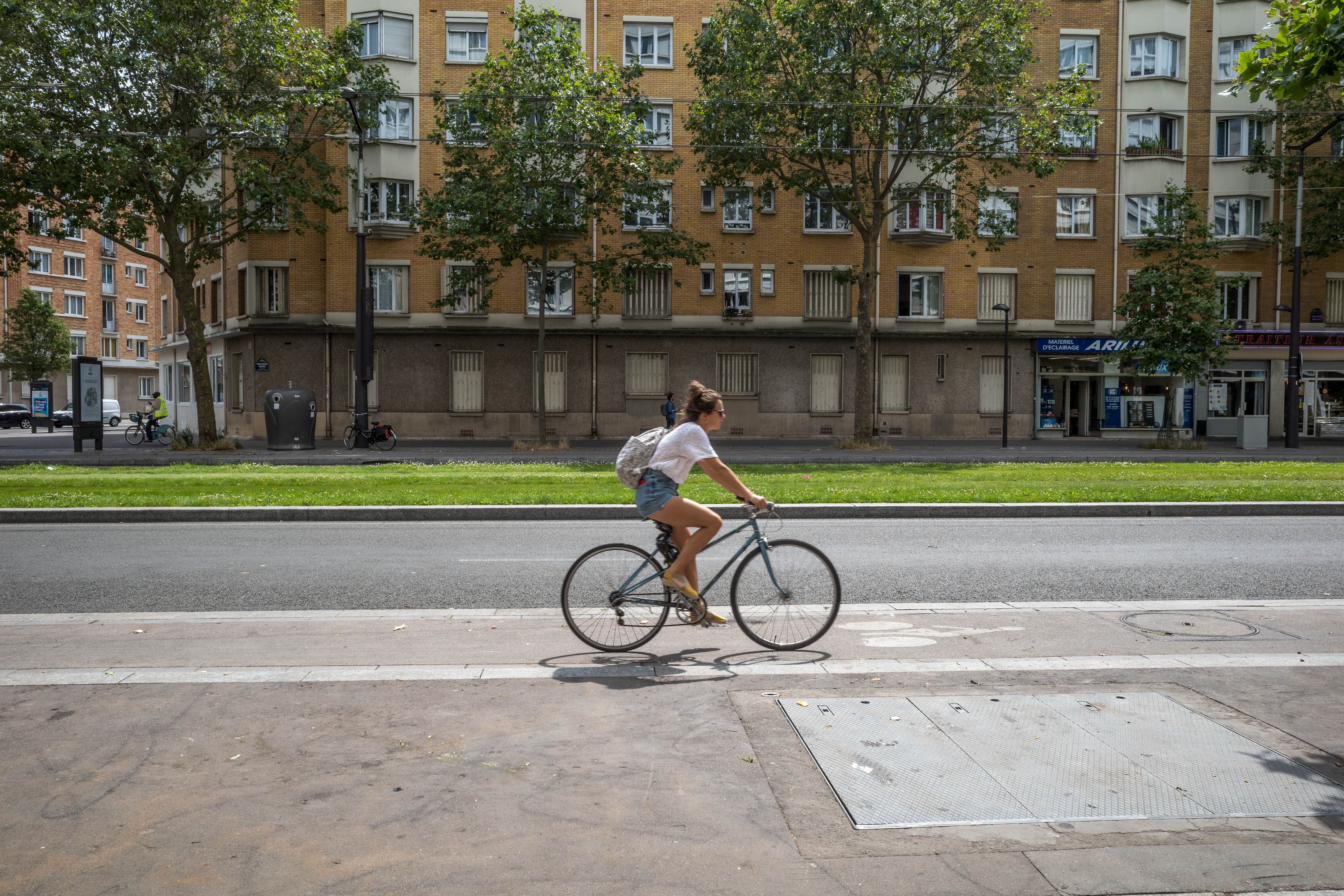 Woman cycling along an urban bike lane beside city buildings, a sustainable alternative to cars