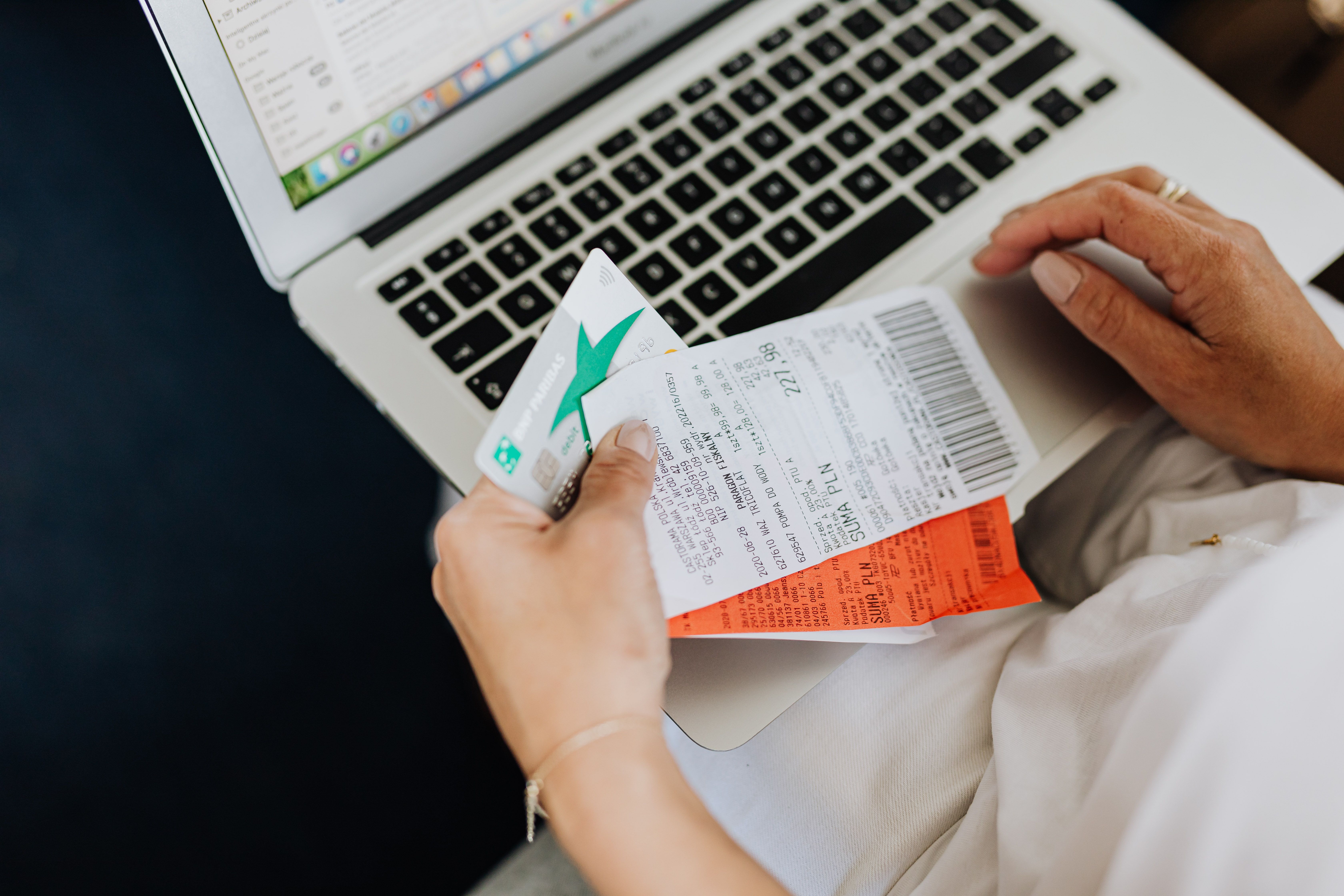 Hands holding receipts and a bank card in front of a laptop, representing online shopping